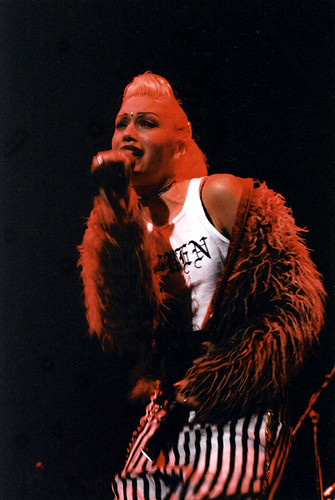 Gwen Stefani, lead singer of No Doubt, croons into a microphone during a concert with her band.  No Doubt has been ingrained in the image of the 90s, but still finds a foothold in modern day culture with their classic song, Just A Girl, identifying the struggles that women face on the daily.  Gwen1 by Kris Sikes is licensed under CC BY-NC-SA 2.0.
